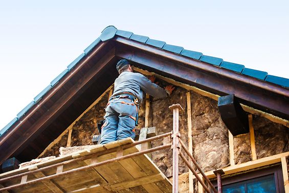Bauarbeiter befestigt Isolationsmaterial an einer Hauswand.