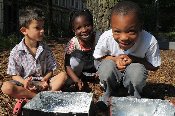Drei Kinder beugen sich lächelnd über selbstgebastelte Solaröfen