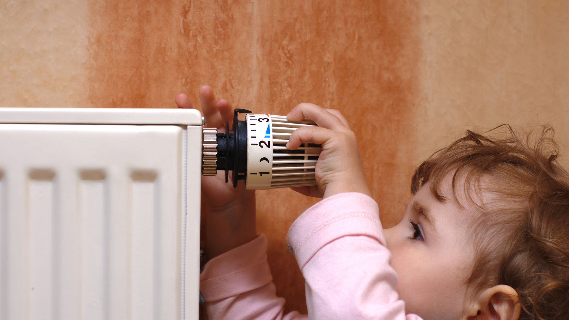 Kleines Kind dreht am Thermostat einer Heizung