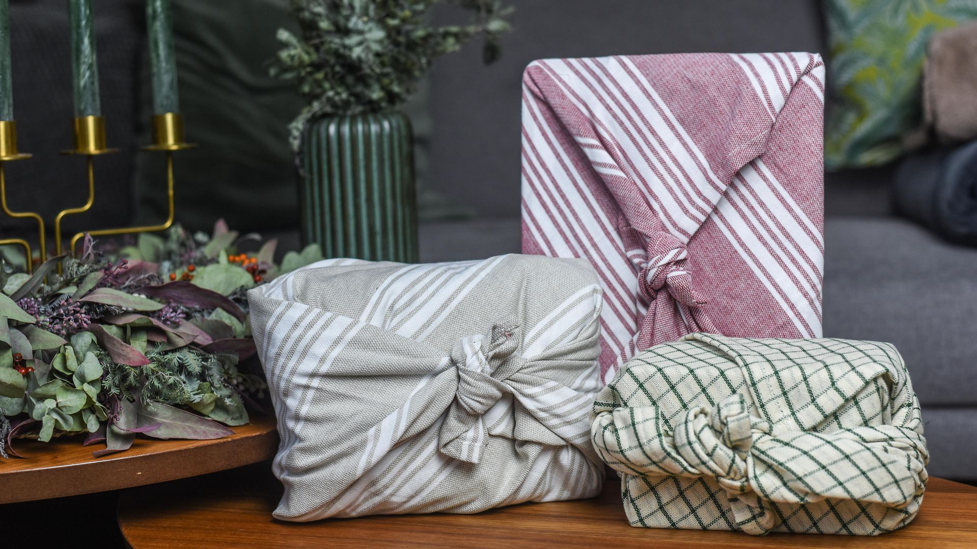 Drei Geschenke sind mit Stoff verpackt und liegen auf einem weihnachtlich geschmückten Tisch.