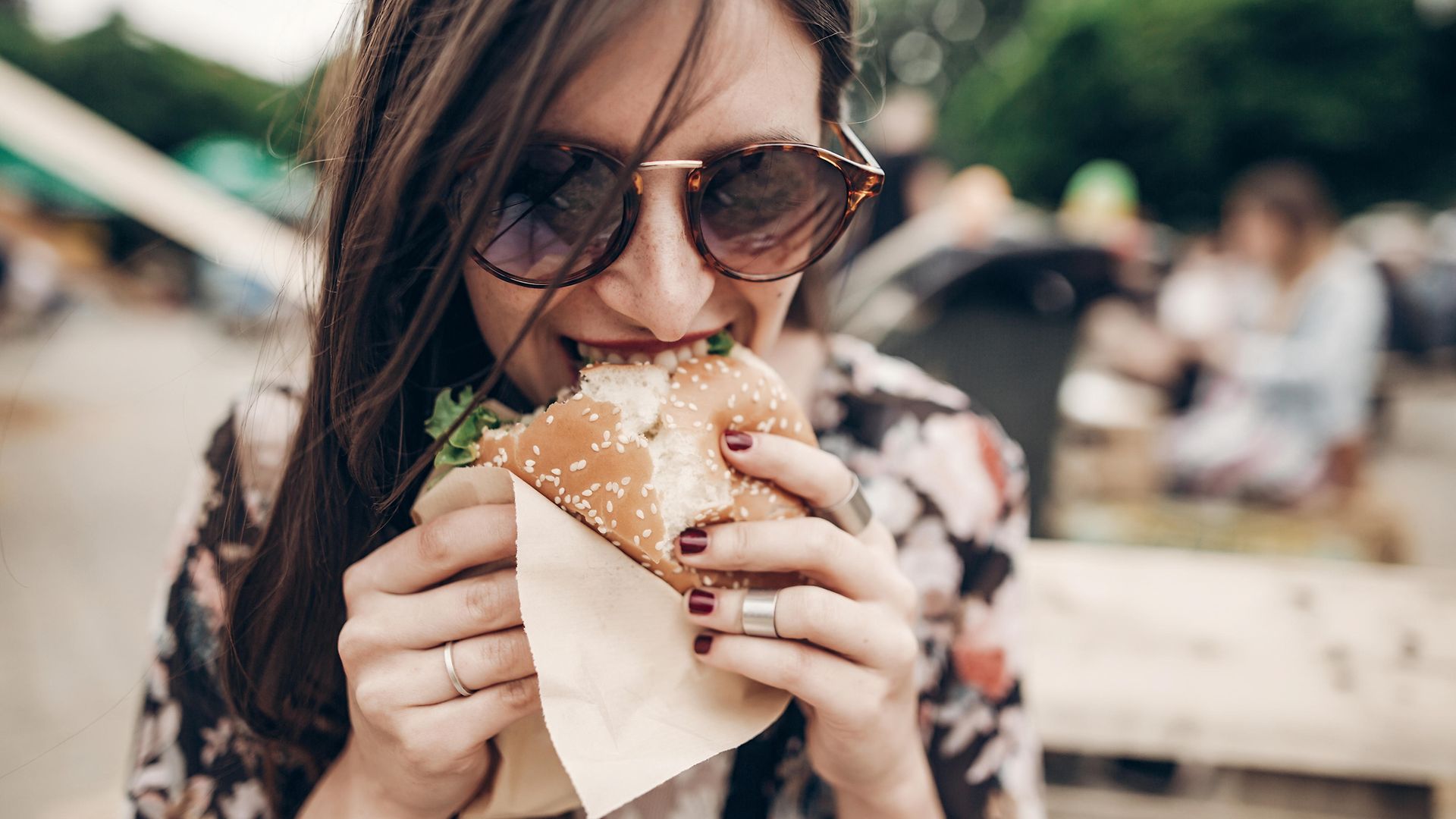 Eine Frau mit Sonnenbrille beißt genussvoll in einen Burger.