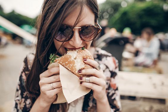 Eine Frau mit Sonnenbrille beißt genussvoll in einen Burger.