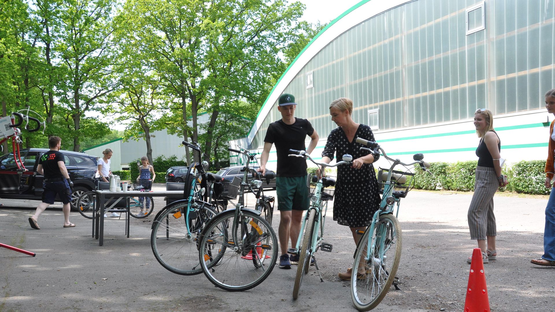 Eine Frau und ein Mann begutachten Fahrräder bei der mobilen Fahrradwerkstatt vor dem Gebäude des Sportvereins THK Rissen